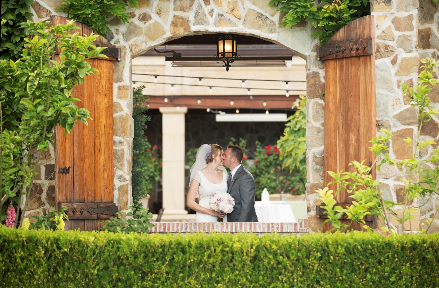 A bride and groom kiss beneath a stone archway